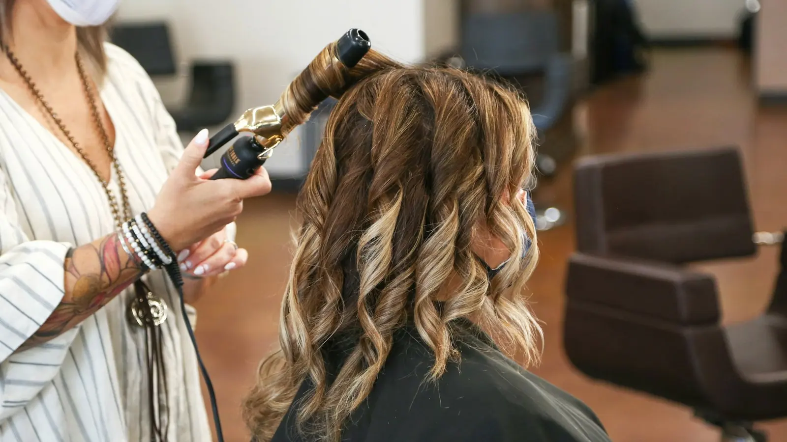 A stylist curling long balayage hair with a gold wand