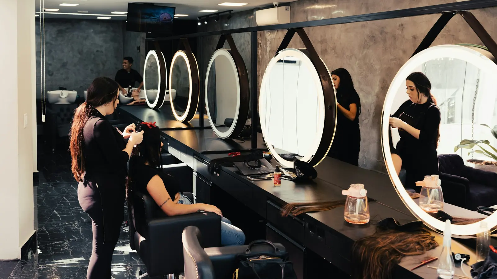 A stylist working at a lit round mirror in a dark modern salon